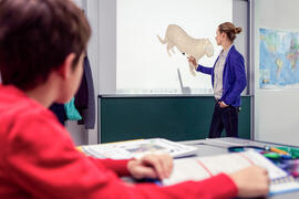 Lehrerin an interaktivem Beamer-Whiteboard mit Stift, Schüler im Vordergrund